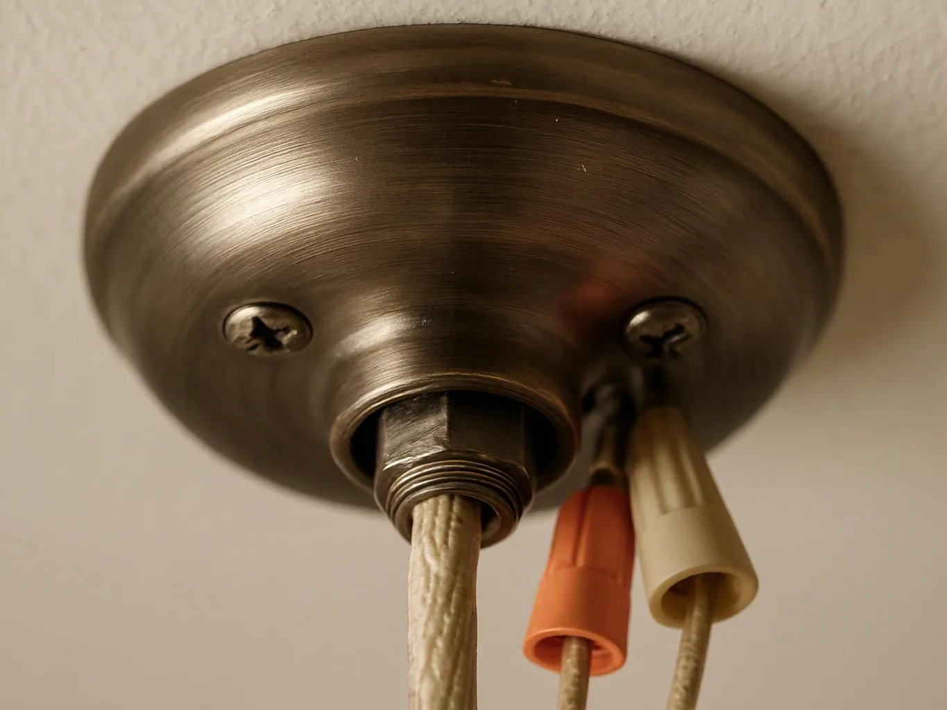 A brass ceiling light canopy hangs against a wall, with three wires and colored wire nuts visible
