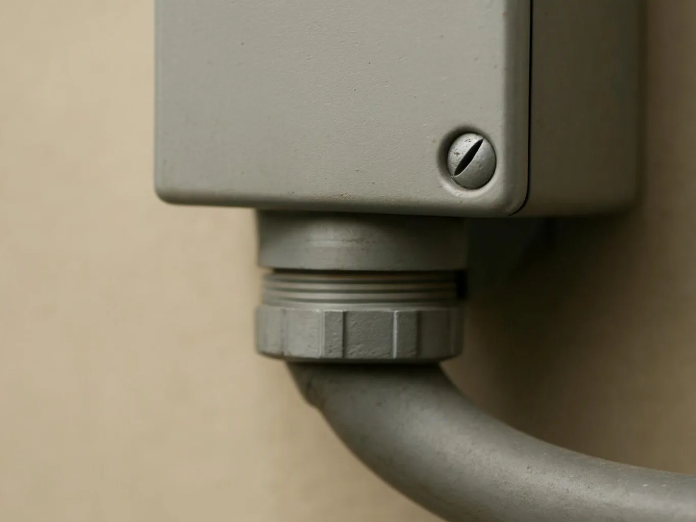 Close-up of a gray electrical junction box with a conduit pipe attached against a beige wall
