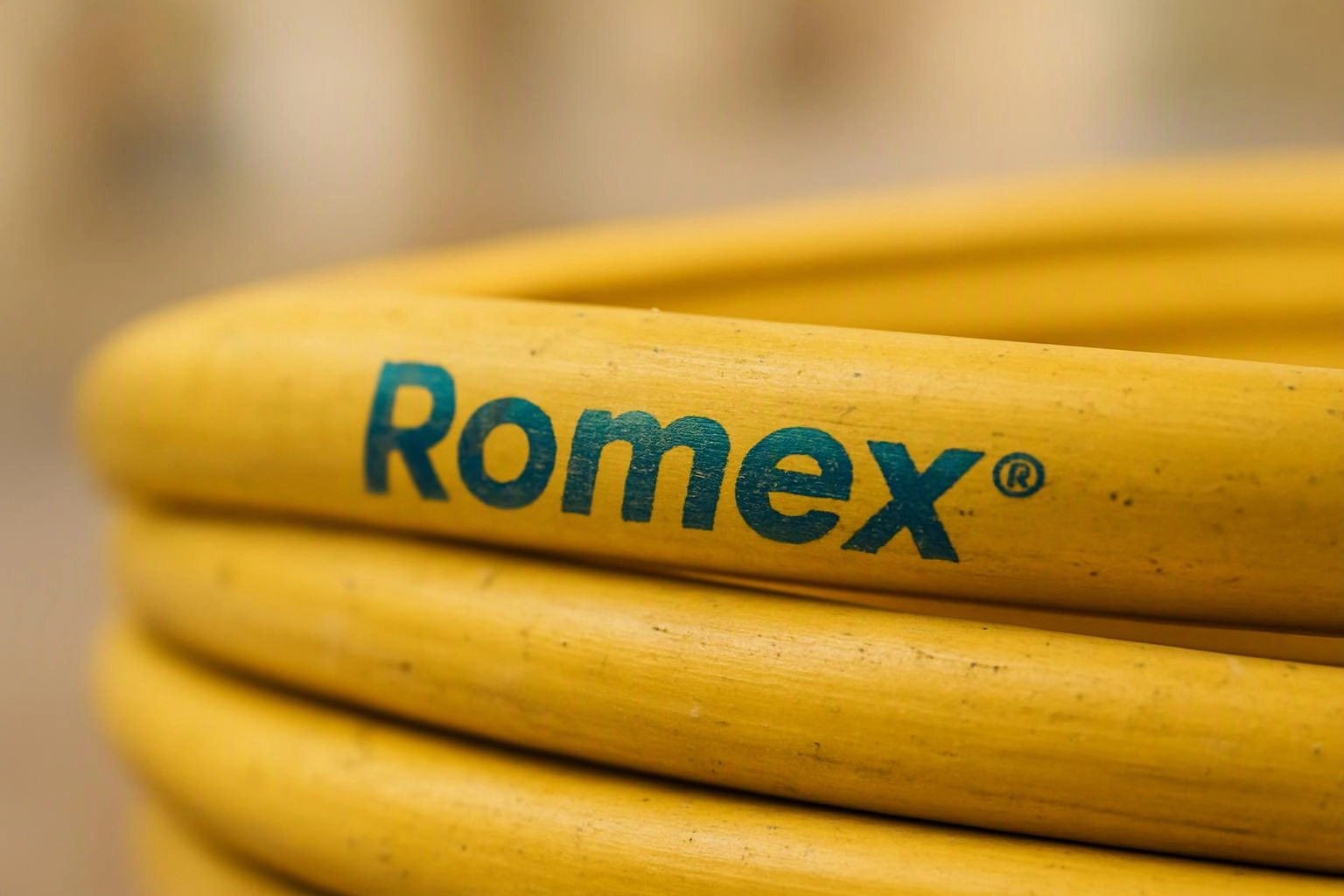 A coiled yellow hose shows the blue word Romex against a blurred indoor background