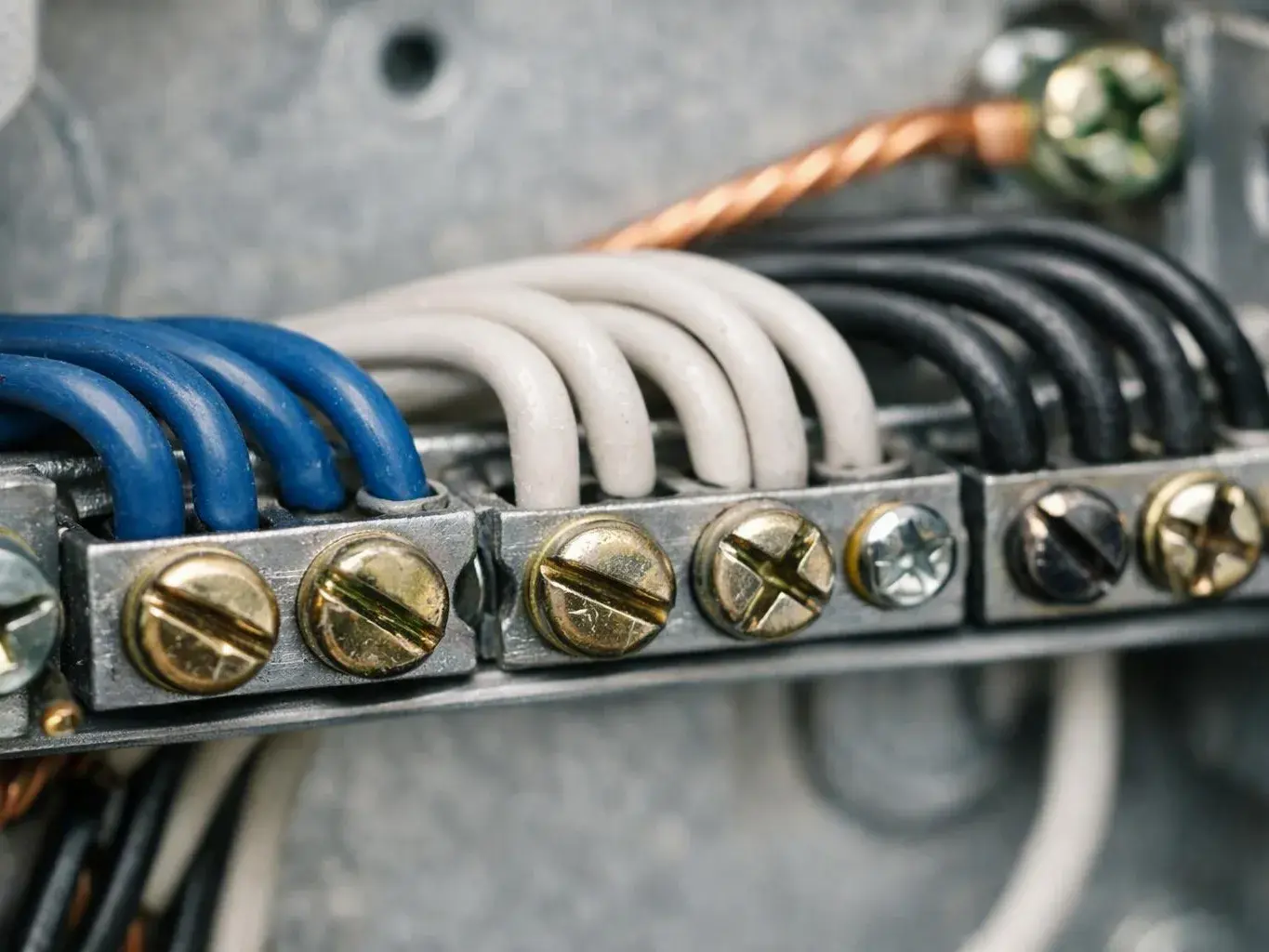 Close-up of electrical wires secured under brass screws inside a gray metal junction box
